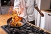 A chef tosses a stir fry with some flames in a frying pan
