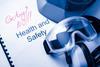 An image showing a health and safety manual on which someone scribbled 'exciting? no!). There are also safety goggles, ear defenders and the edge of a helmet visible