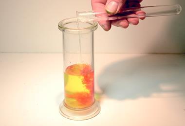 A photograph showing a glass container as potassium iodide solution is added to a lead nitrate solution, leading to an yellow-orange precipitate being formed