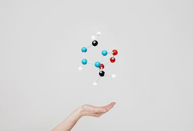 A photographic illustration of a 3D plastic particle model, appearing to float above an open hand