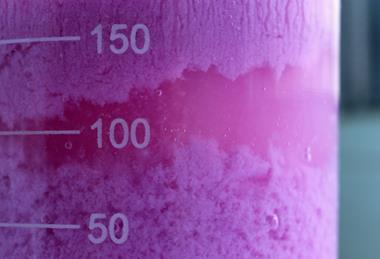 A macro photograph of a glass measuring cylinder containing purple cobalt carbonate formed by a precipitation reaction